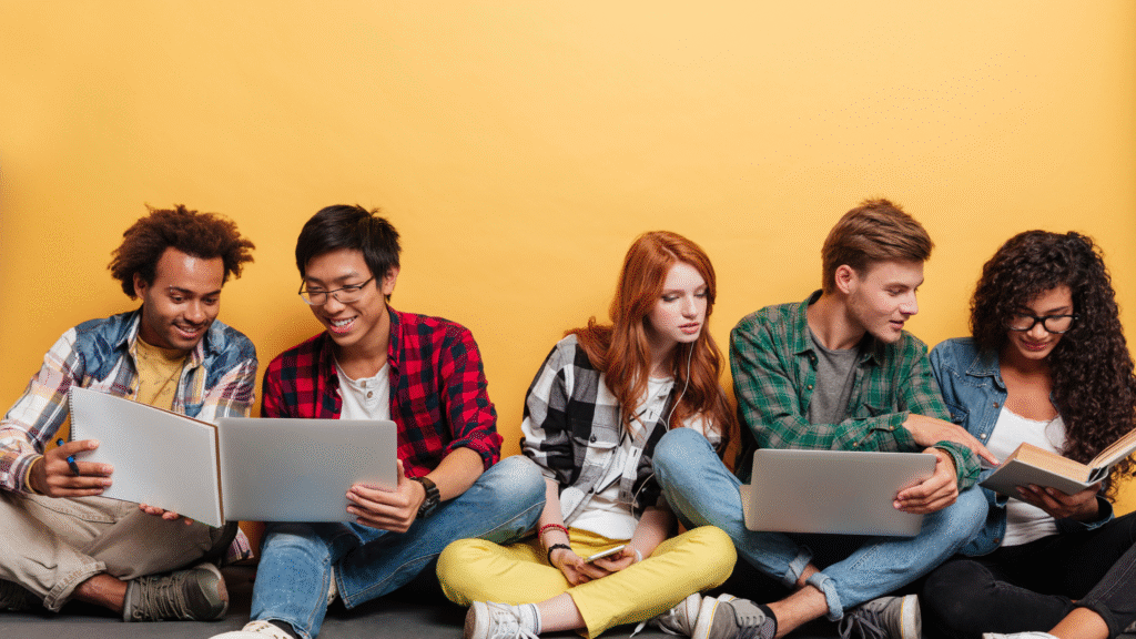 Group of students using laptops and books together, representing collaborative learning.
