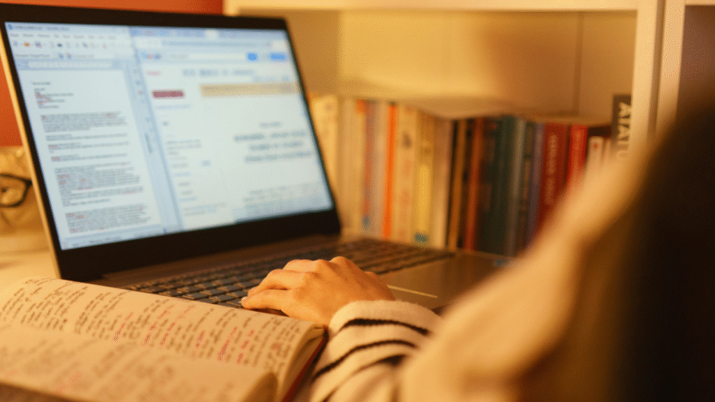 Student studying with a laptop and open book at a desk, illustrating effective and focused study habits.